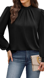 Woman wearing a black blouse with long sleeves and blue jeans, holding a beige clutch.